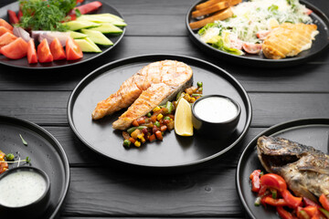 Grilled salmon fish steak with vegetables on black plate. Keto diet concept.