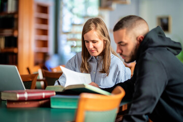 A visually impaired female student and young man sitting in the library and learning together