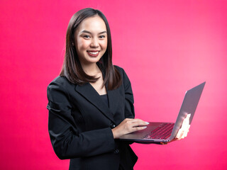 Portrait of an Asian Indonesian woman wearing a black work shirt, working on a laptop. Isolated against a magenta background.