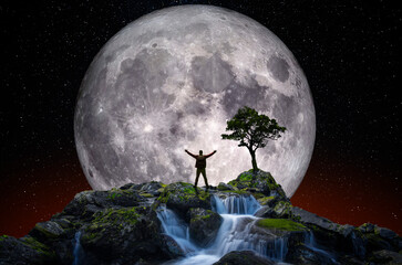 Man on top of a mountain with open arms in front of the full moon