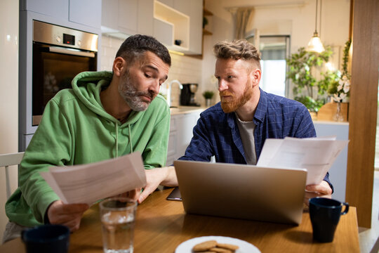 Concerned gay male couple going over bills in the kitchen