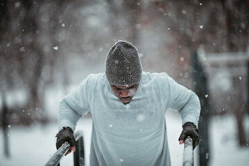 Young fit man doing dips in a outdoor park during snowfall