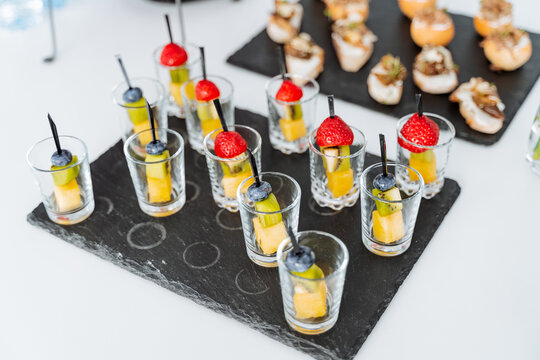 Appetizer cupcakes in a glass, serving food in glassware, skewers with berries and cheese, stone black serving board.