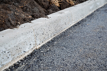 Asphalt-curb joint, laying new road surface, concrete curb, roadbed, black bitumen on the road.