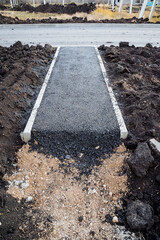 Asphalt road leading to the country house, approach to the gate, asphalt laying, curb, sidewalk, layer of sand and earth.