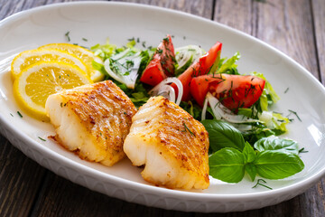 Seared cod loin and fresh vegetables on wooden table
