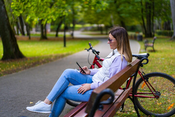 Beautiful woman resting on bench in city park using mobile phone
