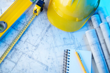 Architect and contractor concept. Rolls with projects. Tool kit of the contractor: yellow hardhat, libella and notebook. 