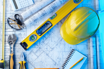 Architect and contractor concept. Rolls with projects. Tool kit of the contractor: yellow hardhat, libella and notebook. 