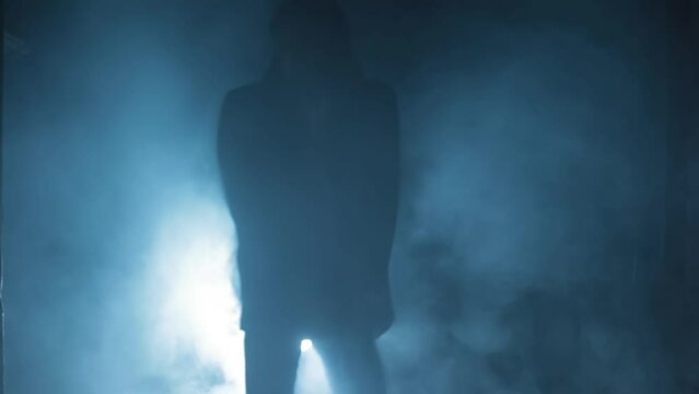 Shot of a young assassin with long hair. A young hitman with long hair coming from the darkness and shooting bullets, Cinematic light, and some smoke. HD footage 24 FPS.