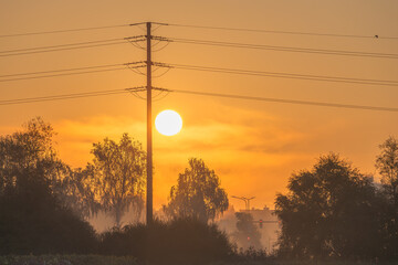 Aufgehende Sonne hinter einem Strommasten im Morgenrot
