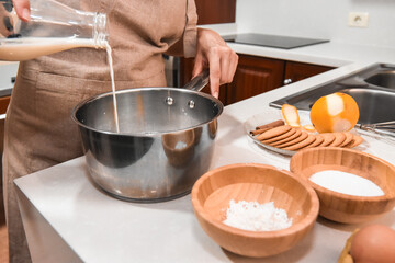 Woman's hand pouring milk into a saucepan to make custard