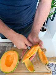 L'uomo passa il taglio del melone con il coltello sul tagliere. Cibo vegetariano e sano. Vista dall'alto. - obrazy, fototapety, plakaty