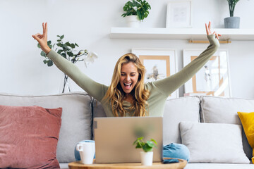 Pretty motivated woman celebrating something while working with laptop sitting on a couch at home