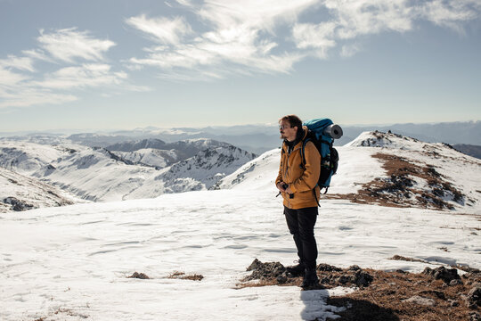 Winter Portrait of a Man with a Backpack: The man stands full-length against a mountain backdrop. High-quality photo for website design, postcards, banners, and travel product advertising.