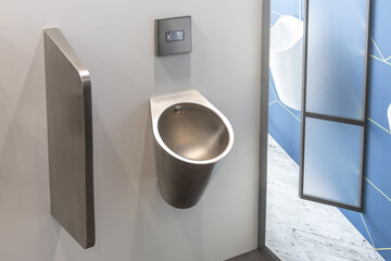 Modern stainless steel urinal installed on a light wall in a public toilet or shopping center....