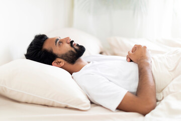 Insomnia Concept. Depressed indian man unable to sleep, lying in bed alone