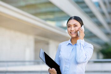 Fototapeta premium Happy Young Korean Business Lady Talking On Cell Phone Outdoors