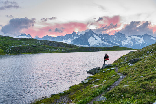 Hiker stands near the shore of Fenetre lake admiring the sunset over the massif of Mount Blanc, Ferret valley, Valais canton, Col du Grand-Saint-Bernard (St. Bernard mountain pass), Switzerland