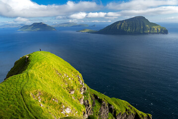 Hiker walks on top of a tall cliff overlooking the ocean, Nordradalur, Streymoy island, Faroe islands, Denmark