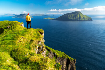 Hiker stands on top of a cliff admiring the rugged view, Nordradalur, Streymoy island, Faroe islands, Denmark