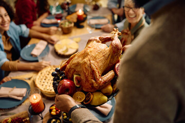 Close up of black man serving Thanksgiving turkey to his extended family at dining table.