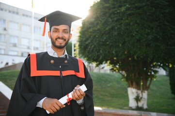 Handsome indian graduate in graduation glow with diploma.