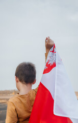 A little boy holds the flag of Poland in his hand. Portrait of a child with a national flag in nature. Rear view. Concept of national holidays and patriotic events. Patriotism. Independence Day