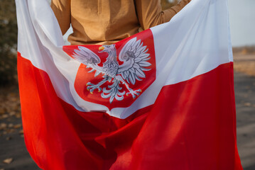 A little boy behind his back is holding the flag of Poland in his hands. Child standing on road...