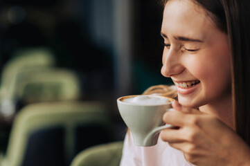A young cheerful woman is laughing while drinking fresh coffee in a coffee shop.