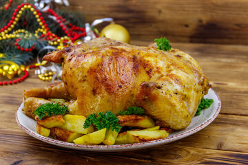 Baked whole chicken with potato and Christmas decorations on a wooden table
