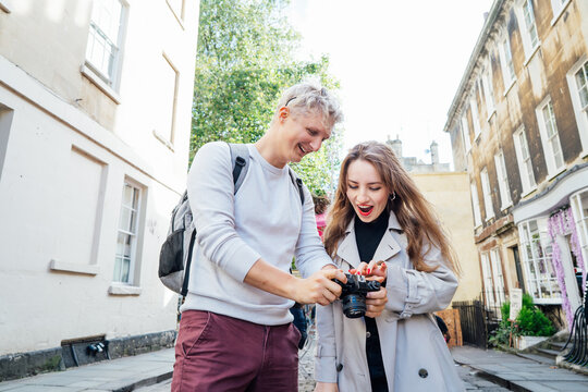 Young emotional friends watching pictures on a digital camera during travel walk in old European city. Tourists taking picture. Professional photographer showing pictures to model outdoors