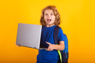 School child using laptop computer. Portrait of school boy isolated on yellow studio background....