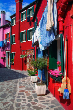 Vibrant coloured buildings in the streets of Burano with clotheslines and household items outside; Burano, Venice, Italy