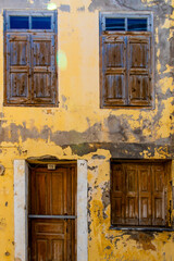 Fototapeta na wymiar An wooden doors and windows in old house Greece. The yellow painted house is weathering away and it’s looking worn.