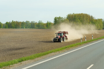 A tractor drives across a plowed field with a cloud of dust behind it.