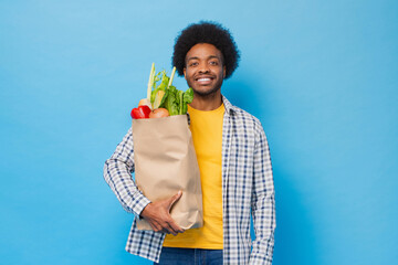 Handsome friendly smiling Afro African American man holding paper shopping bag full of groceries in...