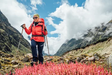 Crédence de cuisine en verre imprimé Makalu Woman in sunglasses with backpack and trekking poles dressed red softshell jacket Calluna heather pink plants during Makalu Barun National Park trek in Nepal. Mountain hiking and active people concept