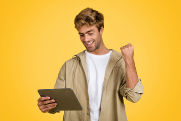Young European man gestures yes with tablet on yellow studio backdrop