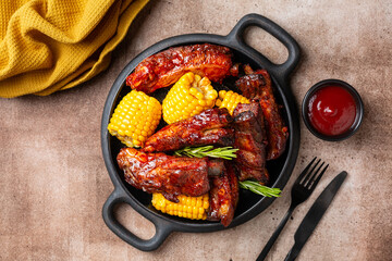 Plate with baked pork ribs with corn cobs, barbecue sauce, rosemary. Brown table background. Meat dinner.