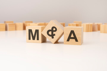 three wooden cubes with M and A symbols on them. white background. in the background there are many wooden blocks of different sizes