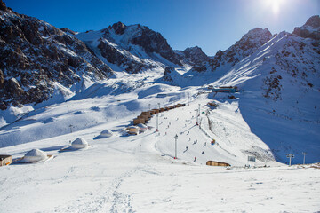 Shymbulak mountain resort's ski slopee with eco hotel, yurts, skiers and snowboarders. Skiers at...