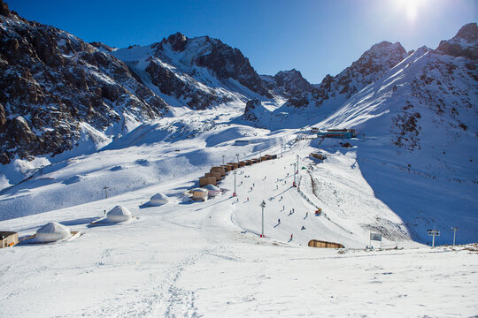 Shymbulak mountain resort's ski slopee with eco hotel, yurts, skiers and snowboarders. Skiers at slopes of ski resort Chimbulak.