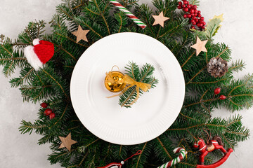 Christmas table setting with gold decoration on white plate on natural fir branches background. Christmas festive decoration serving for Christmas dinner, flat lay, top view