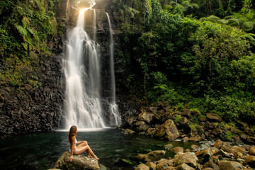 Young woman in bikini sitting by Middle Tavoro Waterfalls in Bouma National Heritage Park, Taveuni Island, Fiji