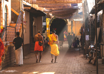 Morning in Gokarna, people walking along a street illuminated by sunlight. Karnataka state, India - obrazy, fototapety, plakaty