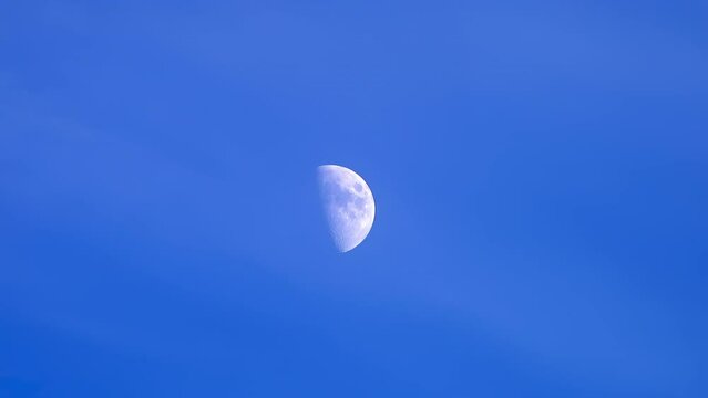A half moon moving across a blue sky with some clouds, half moon at twilight.