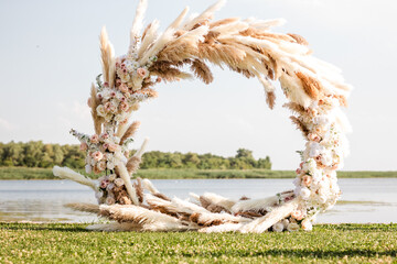 round arch made of pompass grass. outdoor ceremony in summer on the river bank.