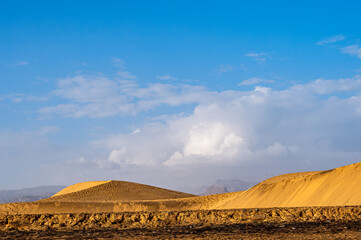 a golden-yellow sunlit dune landscape with a slightly cloudy sky.