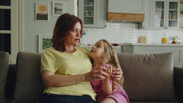 A friendly intelligent mother sits on the sofa in the room with daughter, enthusiastically talks about funny memories, games and events of her infancy. Expressing positive emotions and gesticulation